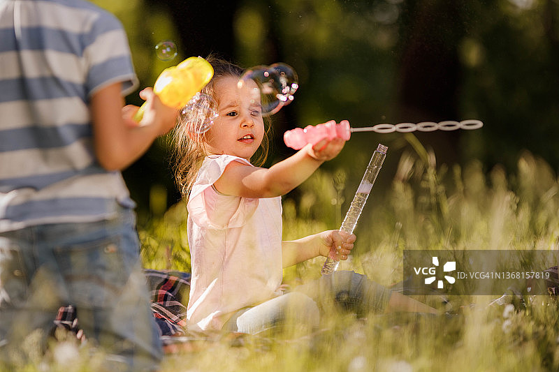 在春日大自然中玩泡泡棒的可爱小女孩图片素材