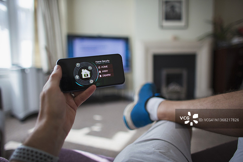 第一人称视角：男人在客厅用智能手机查看家庭安防图片素材