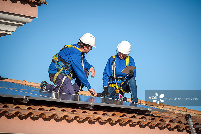 屋顶上跪着修理太阳能电池板的男人和女人工程师图片素材