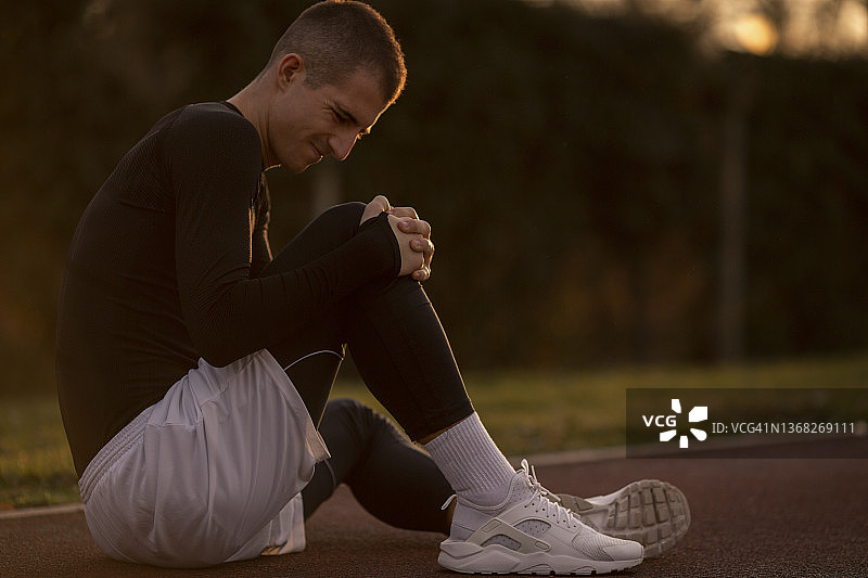 身穿黑色运动服的年轻男子扶着膝盖，感到右膝疼痛图片素材