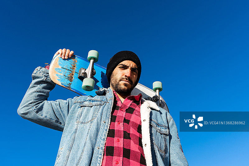 男人肩扛滑板，表情严肃地看着镜头图片素材