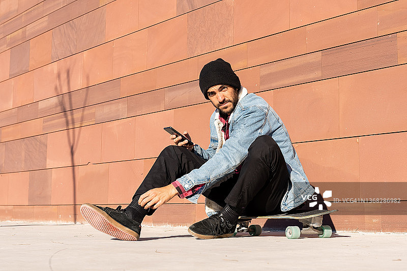 男人坐在滑板上，在街上使用手机图片素材