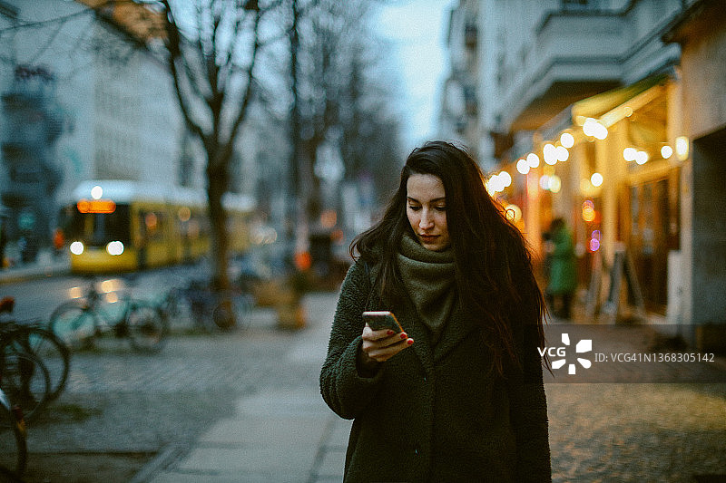 年轻女人走在柏林普伦茨劳贝格时查看手机图片素材
