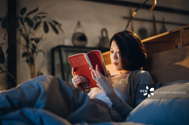 睡前在床上看书的亚洲年轻女子图片素材