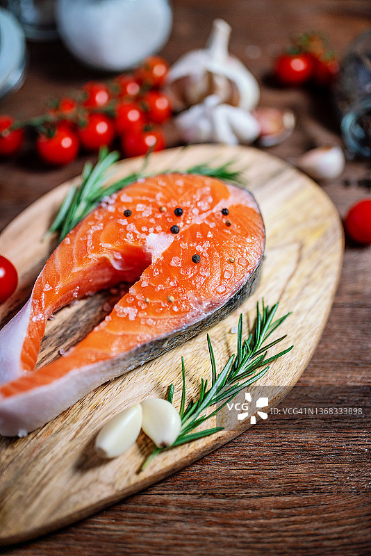 三文鱼：配有番茄、迷迭香和大蒜的生鳟鱼排，置于木桌上图片素材