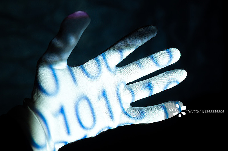 戴着白色手套的手，手掌上呈现基于0和1的二进制代码，代表人类与机器、编程、虚拟世界和未来图片素材