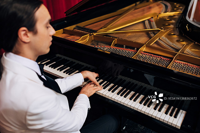 一位年轻钢琴家在音乐表演前练习弹钢琴的背影图片素材