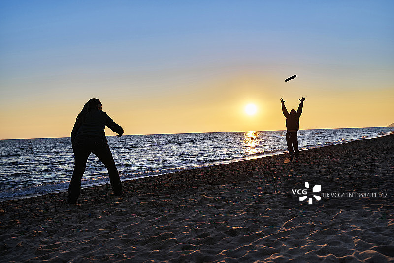 在日落时与妈妈在沙滩上玩飞盘图片素材