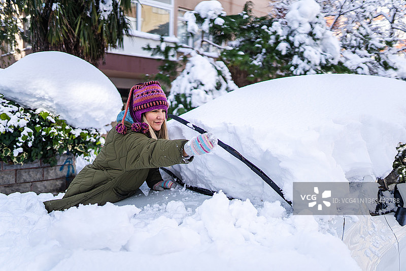 年轻女人穿冬装在车上除雪图片素材