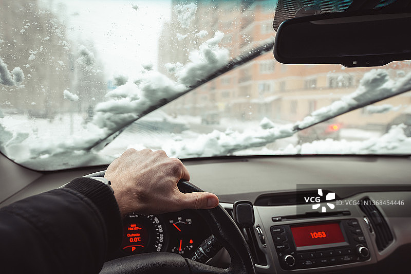 冬季驾驶，雨刮器清除积雪，驾驶员手部和仪表盘内景。城市道路上大雪纷飞图片素材