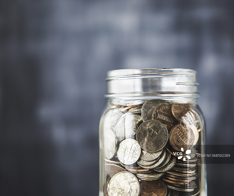 装满美国硬币的玻璃罐，蓝色背景和复制空间。储蓄和金融主题图片素材