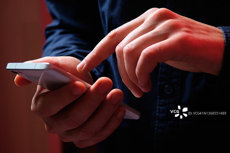 男人手中的手机：一个穿着黑色T恤的年轻男子拿着手机。诈骗犯发送电子邮件。自由职业者，商人。丈夫查看社交网络上的消息和通知。无线技术。图片素材