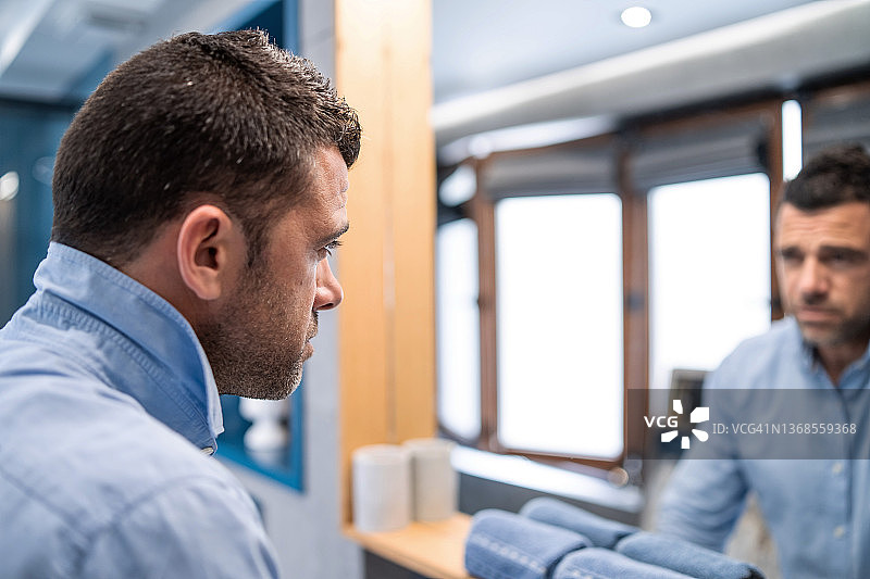 年轻男人穿着蓝色衬衫，在浴室里照镜子，进行晨间护理图片素材