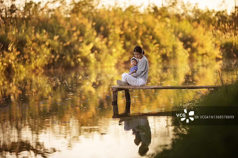 快乐的亚洲母亲在河边拥抱女儿，享受休闲时光图片素材