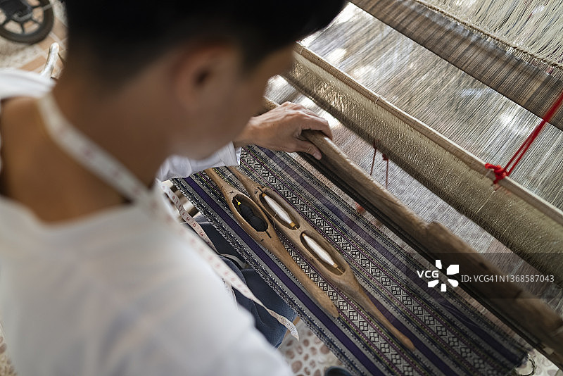 俯视年轻亚洲男子使用传统木制织布机编织土布，实现日常生活的可持续性图片素材