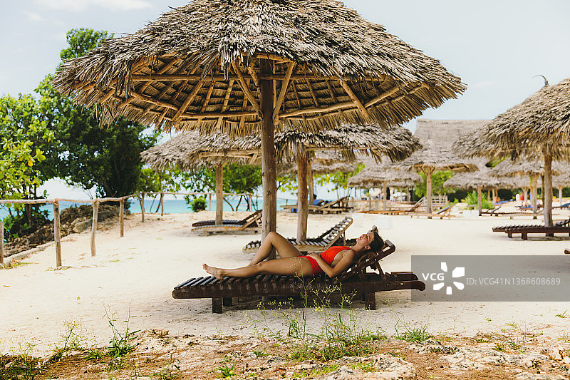 在坦桑尼亚桑给巴尔岛海滩的日光浴床上享受阳光明媚的一天的女旅客图片素材