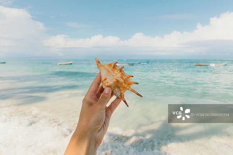 手持海螺，眺望碧绿的海洋和船只的女人图片素材