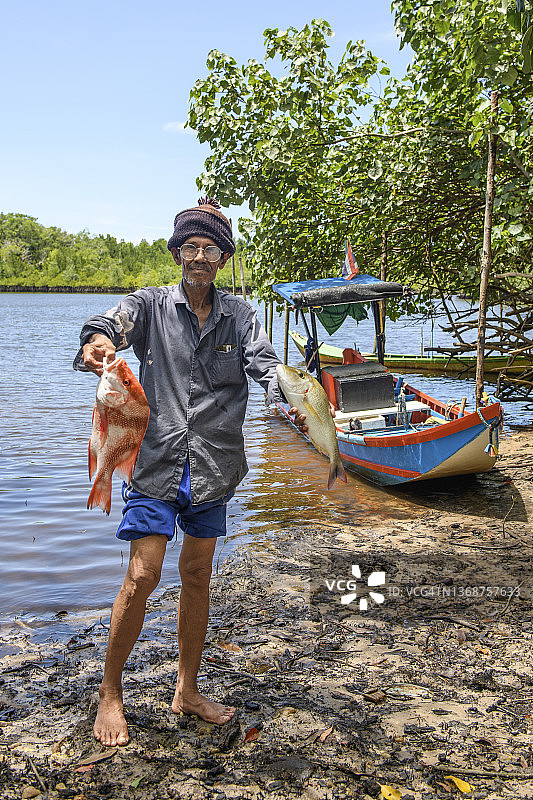 在偏远河流展示渔获的年长亚洲渔民图片素材
