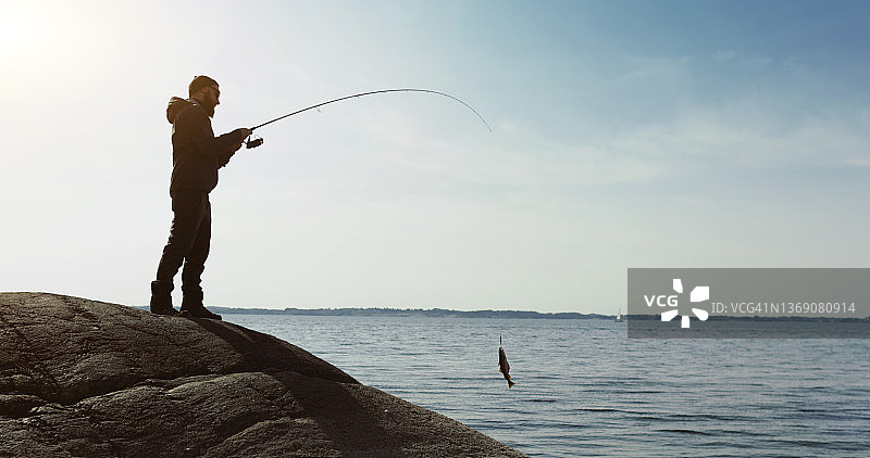 男人在海边的岩石上用钓竿钓鱼图片素材