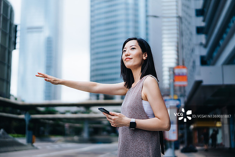 年轻漂亮的亚洲女子在市中心街道上用手机App叫出租车图片素材