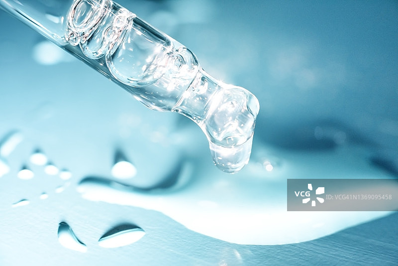 化妆品玻璃滴管吸管，末端带有一小滴透明质酸天然精华液，蓝色背景图片素材