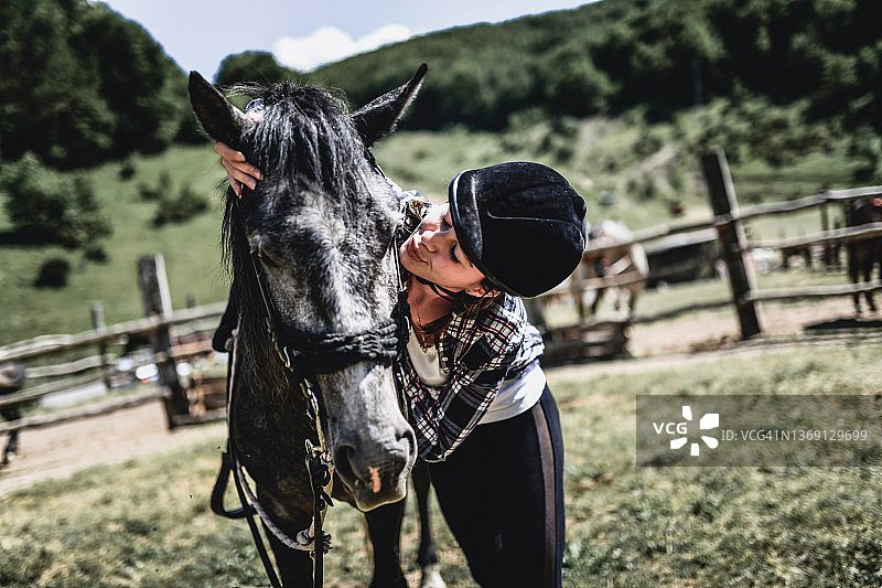 美丽的女人拥抱她的灰色马并准备骑行图片素材
