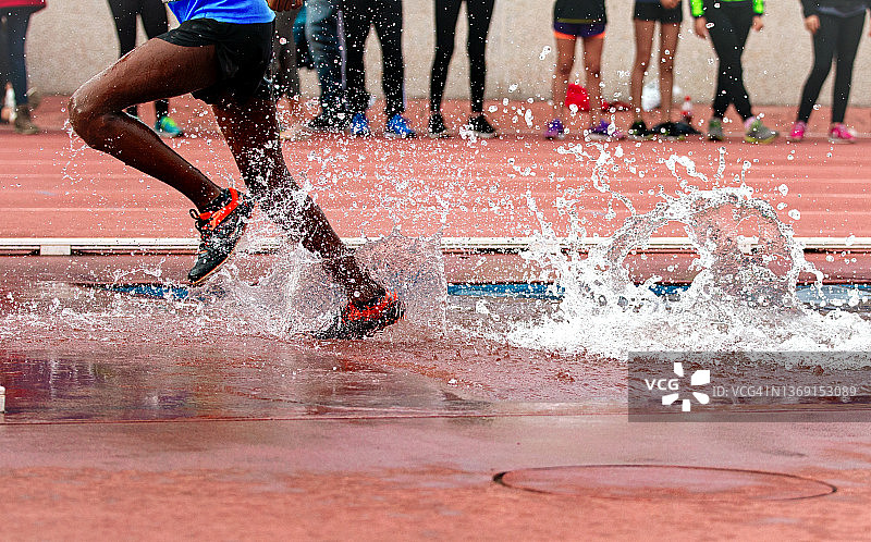 男子参加障碍赛跑，跨越水池时溅起水花图片素材