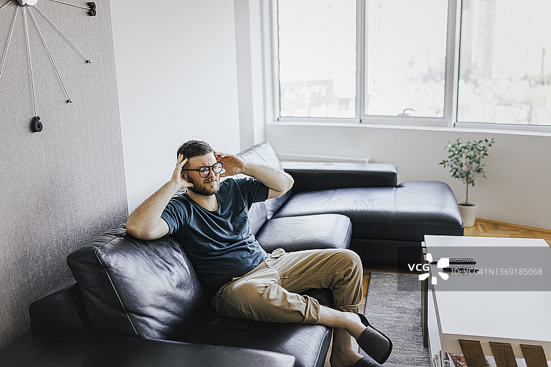 一位坐在客厅沙发上遭受偏头痛的沮丧男人图片素材