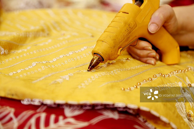 用热熔胶枪将珍珠和珠子粘贴在织物上的手部特写图片素材