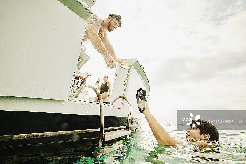 男孩在热带海洋浮潜后在船尾将面罩递给父亲的水上视角图片素材