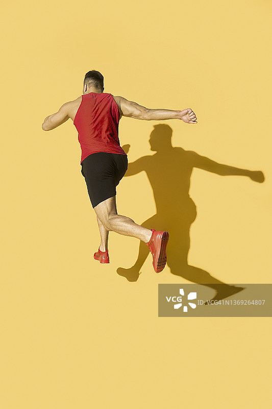 在黄色背景下奔跑的红衣男人，带有阴影图片素材