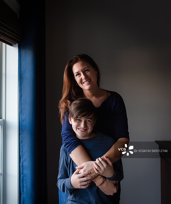 快乐的母子在窗边拥抱微笑图片素材