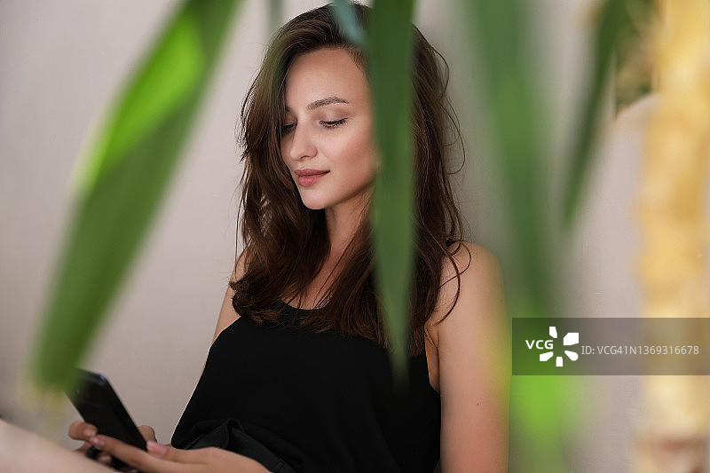 透过树叶拍摄的正在看手机的深色头发女人图片素材