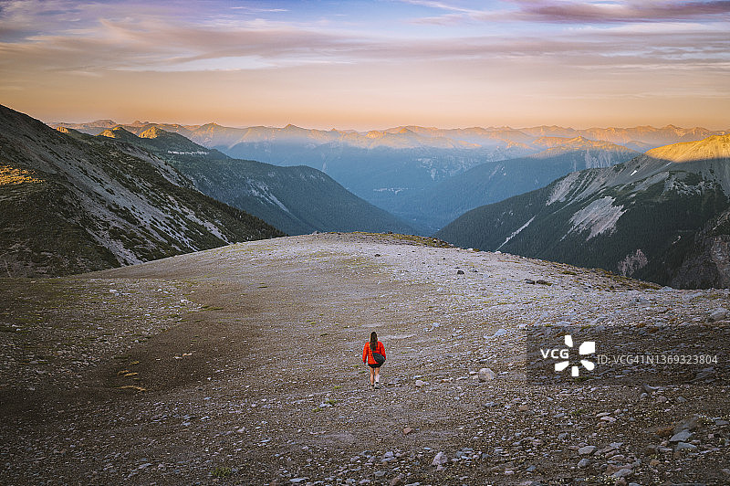 身穿红色夹克的女子在日落时分徒步穿越高山图片素材