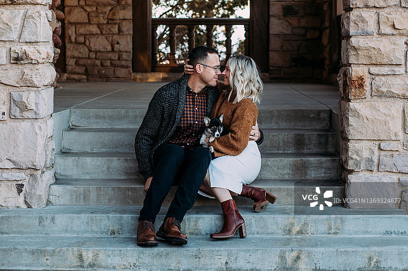 年轻情侣抱着小狗依偎在台阶上图片素材