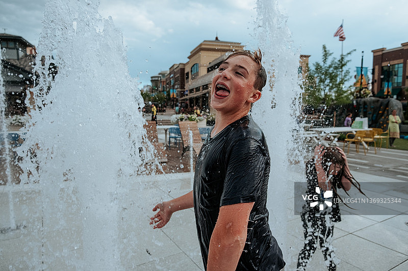 快乐的青少年男孩在夏日喷泉中玩耍图片素材