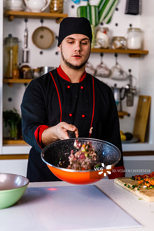 年轻厨师在平底锅中翻炒蔬菜图片素材