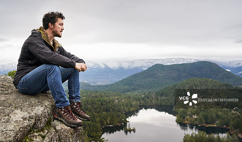 年轻男人坐在岩石上，欣赏风景海岸图片素材