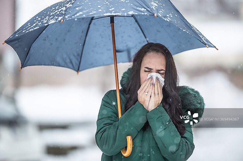 寒冷雪天里，女人拿着雨伞，对着手帕打喷嚏图片素材