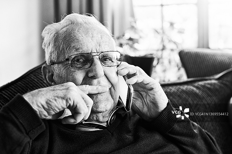 年长的男人坐在客厅里，沉浸在思绪中，听着手机图片素材