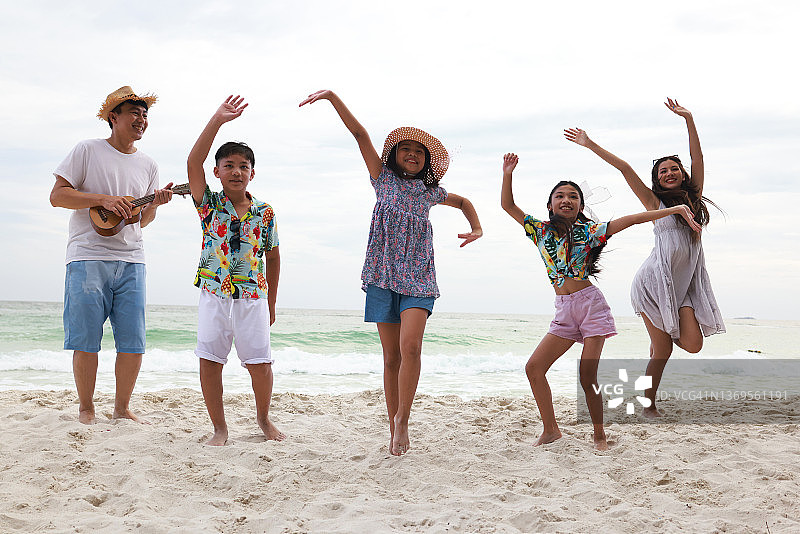 快乐的家庭日，父母和孩子在白色海滩上玩音乐和跳舞，在岛屿海滩上度过暑假图片素材