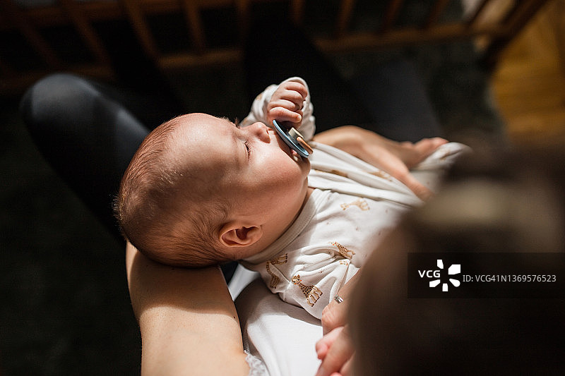 放松的新生婴儿含着奶嘴在母亲怀里图片素材