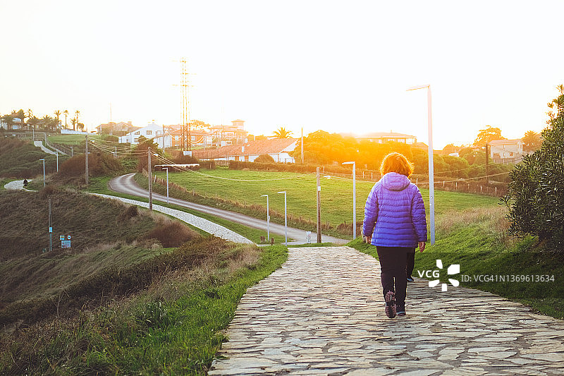 从背后看，女人在黎明时沿着小路行走图片素材