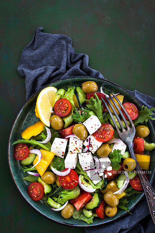 美味的希腊沙拉（新鲜番茄、黄瓜、甜椒、洋葱、橄榄和羊乳酪），俯视，深绿色背景图片素材
