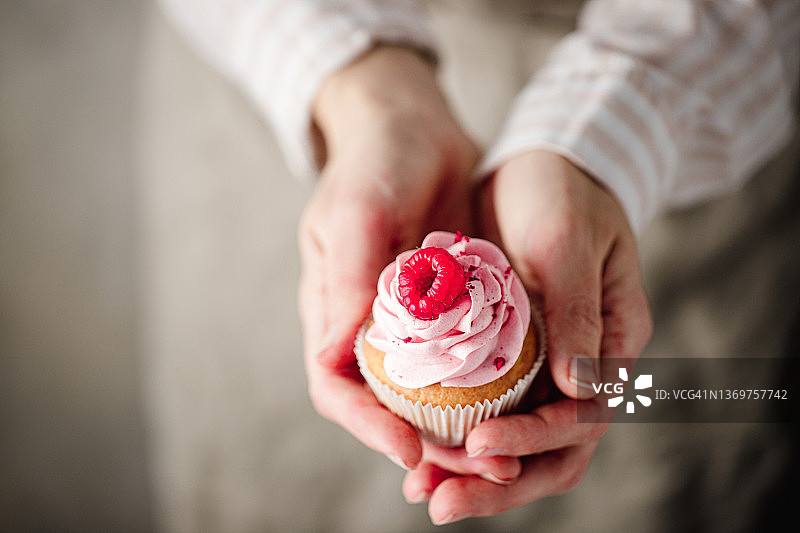 女人拿着覆盆子纸杯蛋糕的特写图片素材