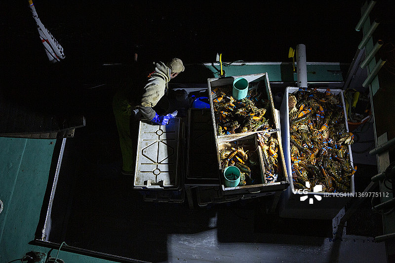 夜间拍摄的满载新鲜龙虾的龙虾船，一名工人在船上作业图片素材