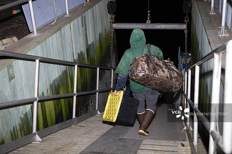 渔民晚上走在木板路上，扛着大袋子和龙虾箱图片素材