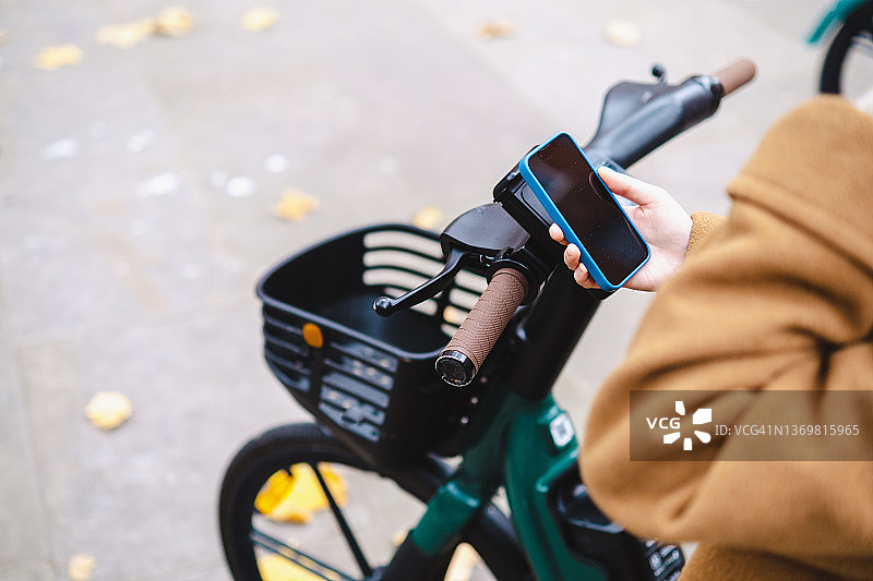 女人用智能手机租电动自行车图片素材