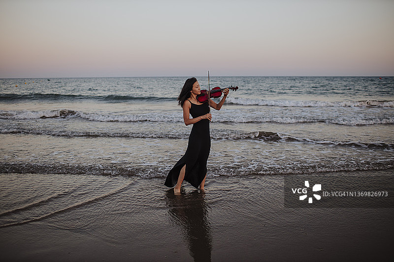 日落时分，在海边拉小提琴的女人图片素材