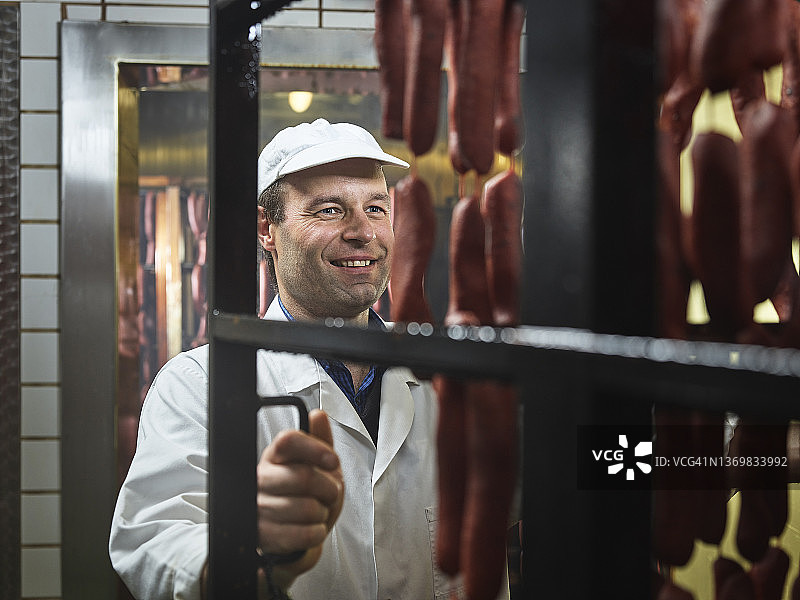 微笑的屠夫从屠宰场的熏制室里取出香肠图片素材